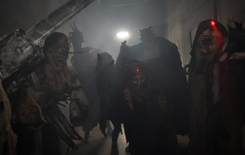 A group of eerie, masked figures with glowing red lights in a dark, foggy corridor, creating a spooky atmosphere.