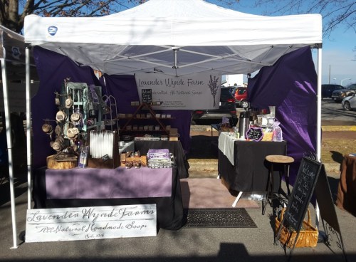 A market stall for Lavender Wylde Farm featuring lavender products, handmade crafts, and a purple-themed display.
