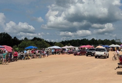 A bustling outdoor market with colorful tents, vendors, and shoppers on a sunny day.