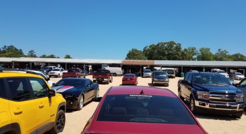 A parking lot filled with various cars under a clear blue sky, with a building in the background.