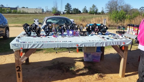 A table displaying various jewelry pieces, including necklaces and bracelets, set up outdoors with cars in the background.