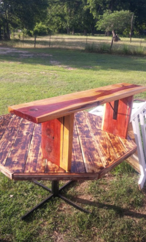 A rustic wooden bar table with a unique octagonal base, set on a grassy outdoor area.