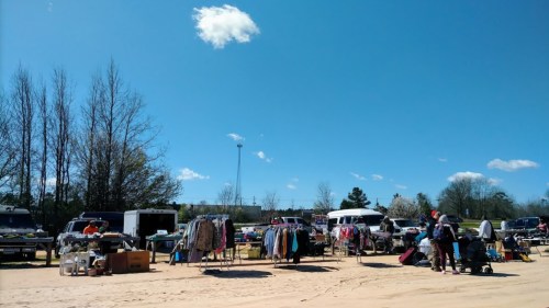A vibrant outdoor market with clothing and goods for sale under a clear blue sky and scattered clouds.