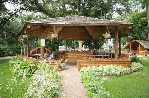 A wooden gazebo surrounded by greenery and flowers, with hanging plants and a stone pathway leading to it.