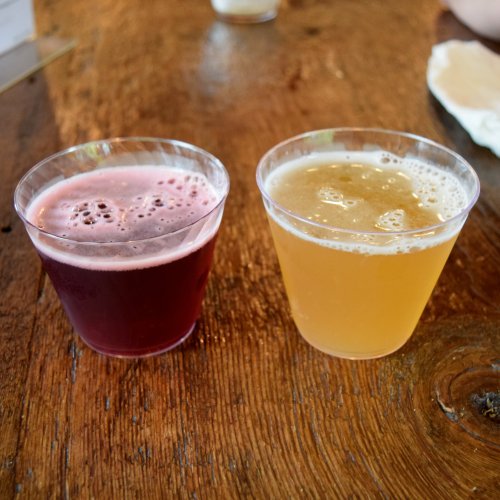 Two plastic cups on a wooden table: one filled with dark red beverage, the other with a light golden drink.