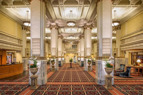 Elegant hotel lobby featuring tall columns, ornate ceilings, and a patterned carpet with floral arrangements.