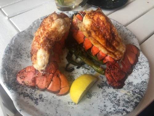 A plate of grilled lobster tails on a bed of greens, garnished with a lemon wedge.