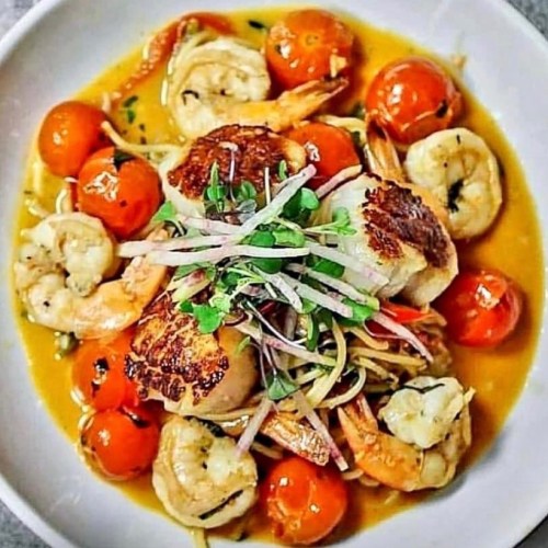 A bowl of seafood pasta featuring shrimp, scallops, cherry tomatoes, and herbs in a flavorful sauce.