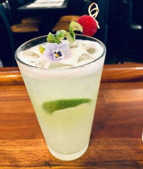 A refreshing cocktail in a tall glass, garnished with a raspberry, lime, and a flower on top.