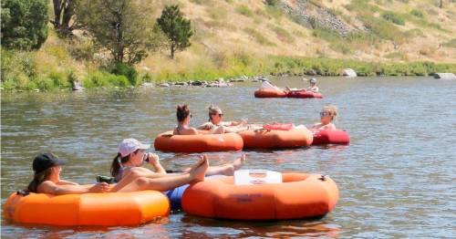 People relaxing on inner tubes in a river, enjoying a sunny day surrounded by greenery and hills.