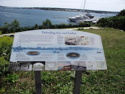 Sign about the historical significance of a harbor, with a view of water and boats in the background.