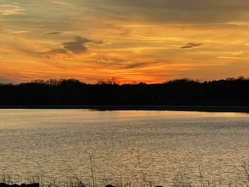 A serene sunset over a calm lake, with vibrant orange and yellow hues reflecting on the water's surface.