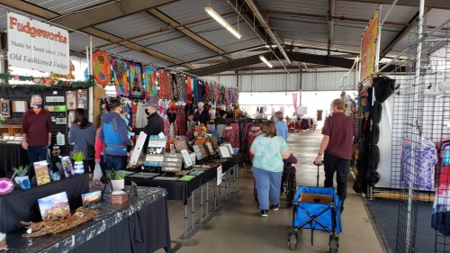 A bustling indoor market with vendors selling handmade crafts, colorful displays, and shoppers browsing the stalls.