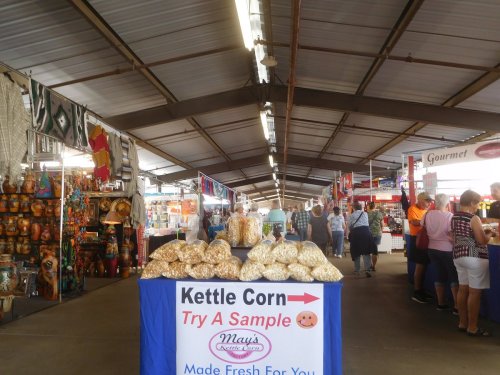A bustling market with vendors selling goods, featuring a kettle corn stand inviting samples.