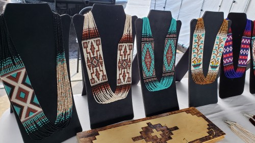 Colorful beaded necklaces displayed on black stands, showcasing intricate patterns and designs at a market.