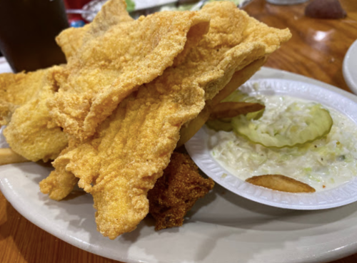 A plate of golden fried fish fillets with a side of coleslaw and pickles.