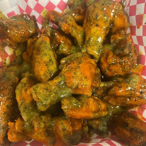 A close-up of spicy chicken wings coated in a vibrant orange sauce, served in a red and white checkered basket.