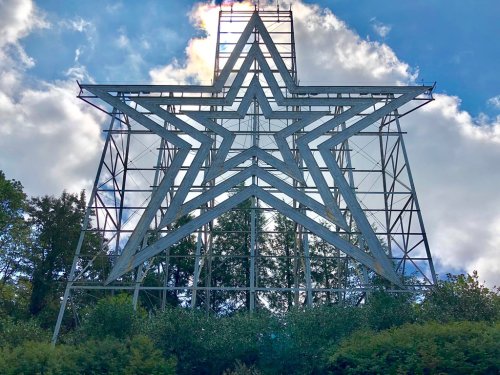 A large white star structure on a hillside, surrounded by trees and under a blue sky with clouds.