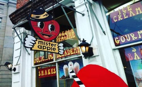 A colorful sign for "Mister Apple" featuring a smiling apple character outside a shop with vintage-style window displays.
