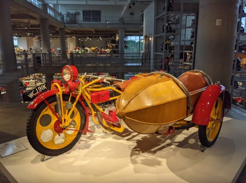 A colorful vintage motorcycle with a wooden sidecar, displayed in a museum setting.