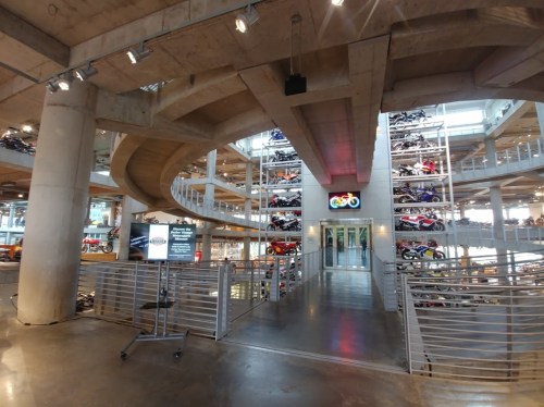 Interior view of a modern multi-level motorcycle showroom with bikes displayed on various levels and a spiral staircase.