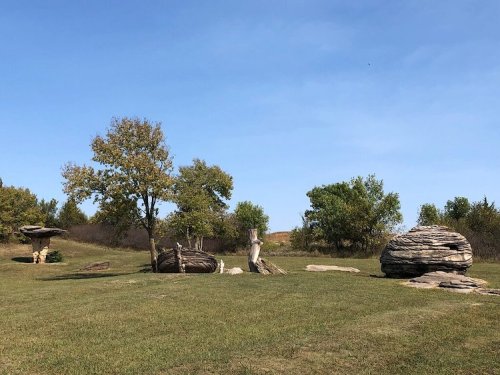 A grassy landscape featuring unique rock formations and a few scattered trees under a clear blue sky.