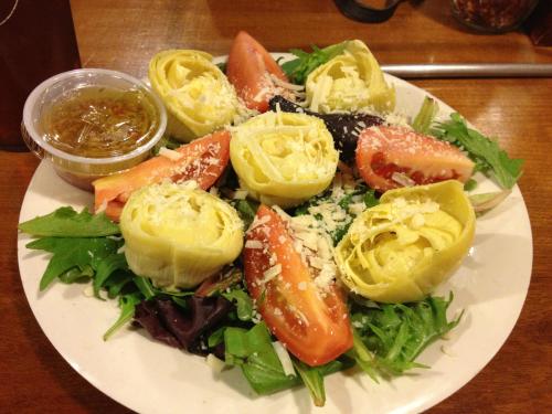 A fresh salad with artichoke hearts, tomatoes, mixed greens, and a side of dressing.