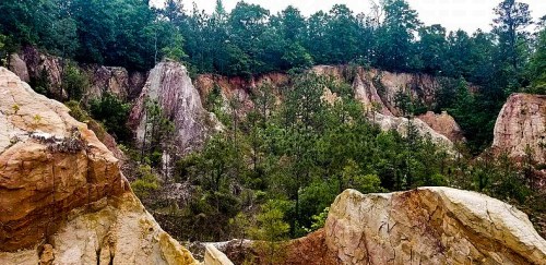 A scenic view of colorful rock formations surrounded by lush green trees and a steep, rugged landscape.