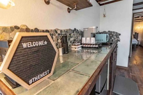 A cozy kitchen counter with a welcome sign, coffee maker, and various kitchen appliances against a stone backsplash.