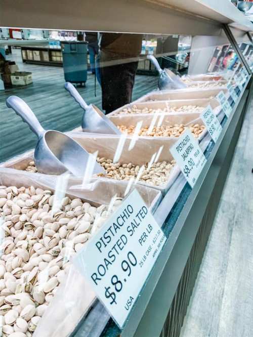 Display of various nuts in bins, with a focus on roasted salted pistachios priced at $8.90 per pound.