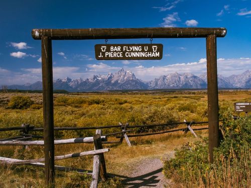 Sign for Bar Flying U J. Pierce Cunningham with mountains in the background and a clear blue sky.