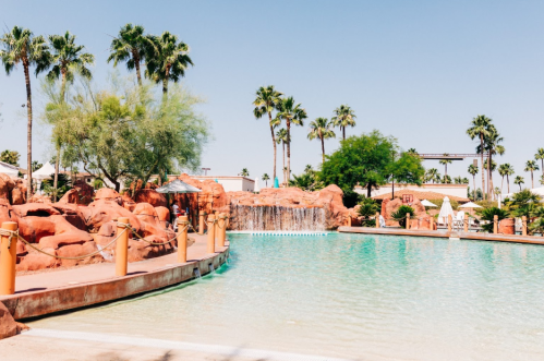 A serene pool area surrounded by palm trees and red rock formations under a clear blue sky.