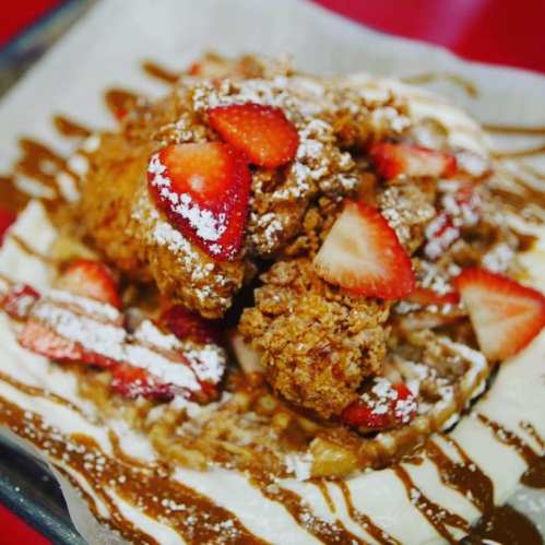 A delicious dish featuring fried chicken topped with strawberries and powdered sugar, served on a bed of creamy sauce.