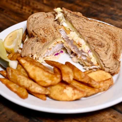 A sandwich with layers of chicken and coleslaw, served with crispy potato wedges and a lemon wedge on the side.