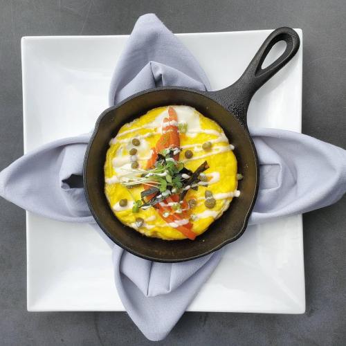 A cast iron skillet with a fluffy omelet topped with tomatoes, herbs, and drizzled sauce, resting on a folded napkin.