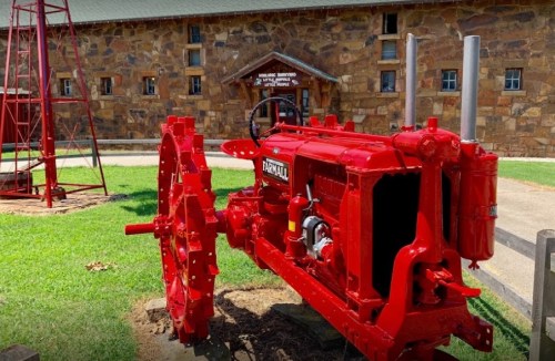 A bright red vintage tractor displayed on green grass in front of a stone building.