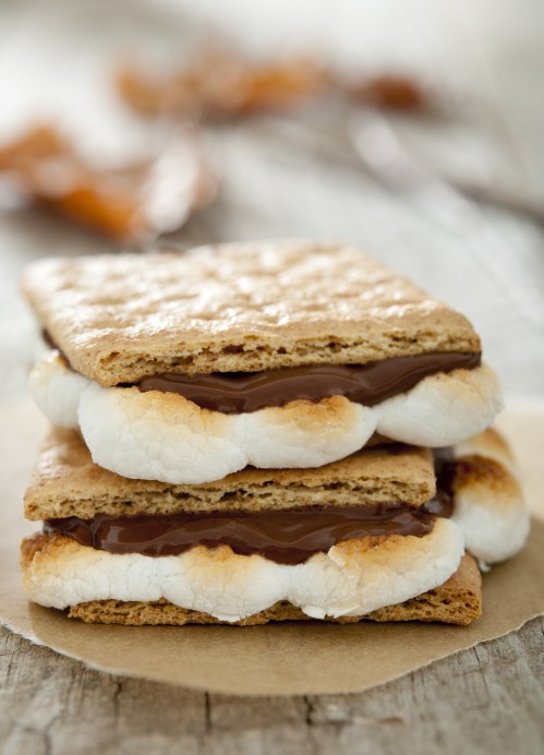 Three s'mores stacked on a wooden surface, featuring graham crackers, melted chocolate, and toasted marshmallows.