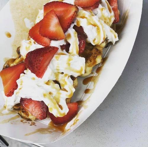 A dessert featuring a waffle topped with whipped cream, fresh strawberries, and drizzled with caramel sauce.