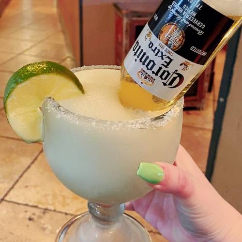 A margarita glass with a salted rim, topped with a Corona beer and a lime wedge.