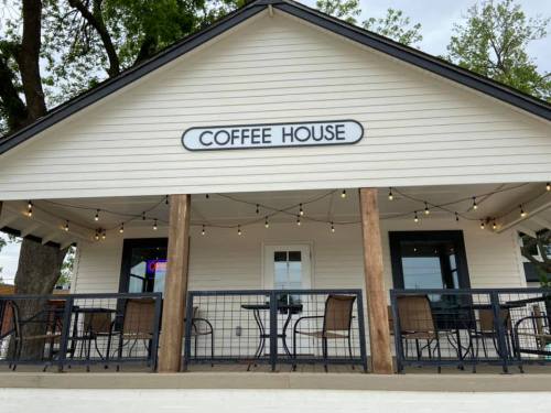 A cozy coffee house with outdoor seating and string lights, featuring a welcoming porch and a sign that reads "COFFEE HOUSE."