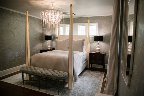 A stylish bedroom featuring a four-poster bed, elegant chandelier, and decorative wallpaper.