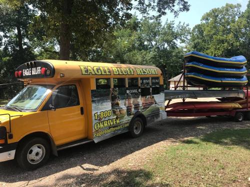 A yellow bus with "Eagle Bluff Resort" signage parked next to a trailer carrying stacked kayaks and canoes.