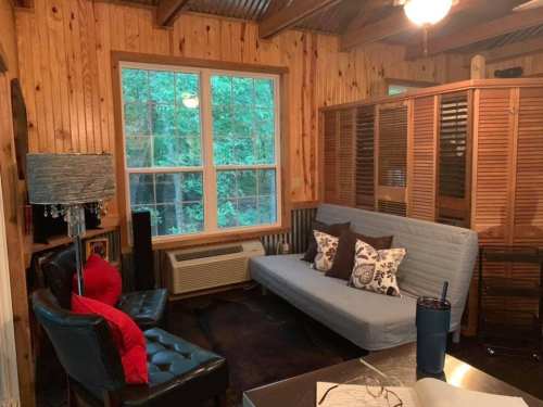 Cozy room with wooden walls, a blue sofa, black chairs, and a window overlooking greenery.