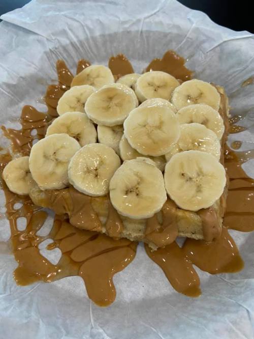 A slice of bread topped with peanut butter and banana slices, drizzled with honey, on a paper plate.