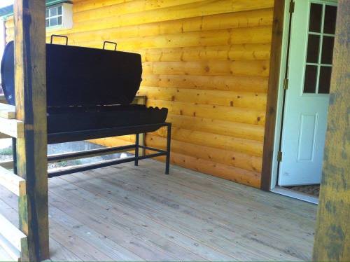 A wooden porch with a large black grill and a white door leading inside a log cabin.