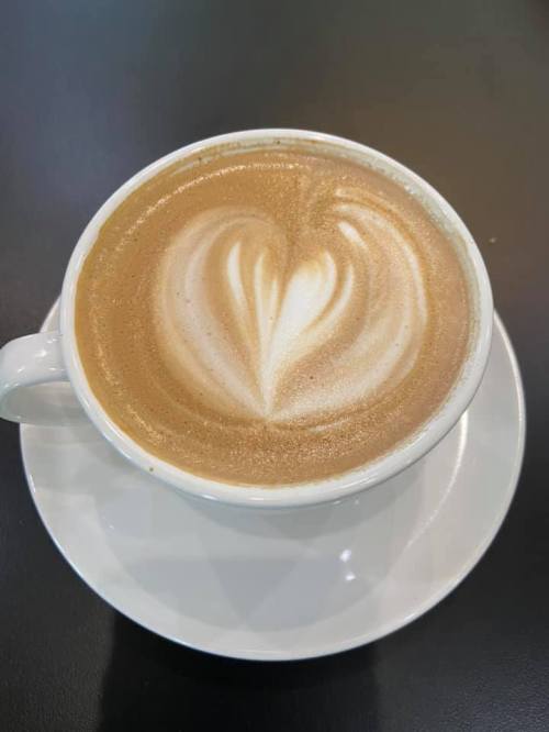 A cup of latte with a heart-shaped foam design, placed on a white saucer against a dark background.