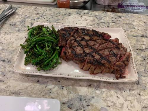 A perfectly grilled steak with crosshatch marks, served alongside sautéed broccolini on a white plate.