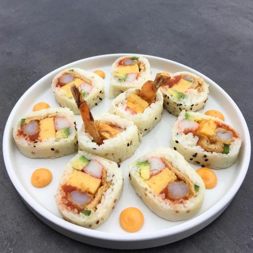 A plate of sushi rolls with shrimp, egg, and colorful fillings, garnished with orange sauce dots.