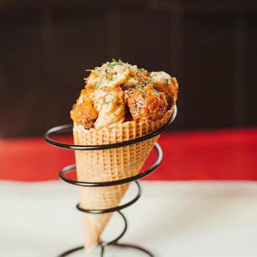 A waffle cone filled with crispy fried chicken, topped with sauce and herbs, served in a metal holder.