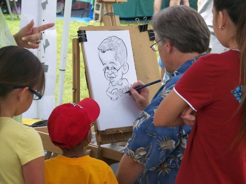 A caricature artist draws a smiling boy while two children watch, enjoying the outdoor event.